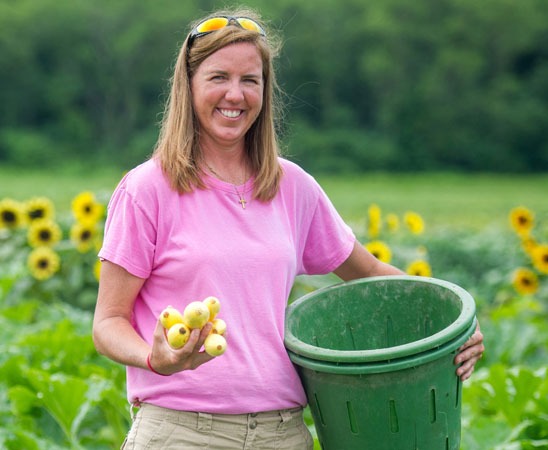 Farm to Food Bank Coordinator Amy Cawley smiles while harvesting fresh produce from a local farm
