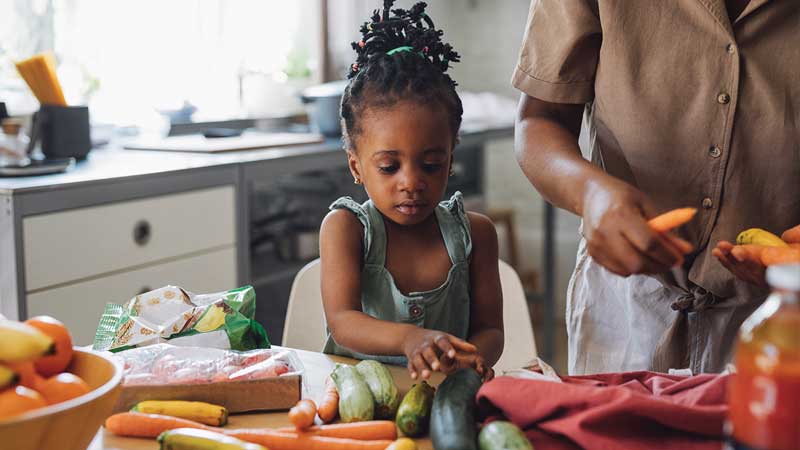 black child helps prepare produce in kitchen