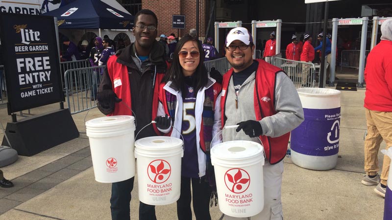 three volunteers holding Ravens Food and Funds Drive donation buckets