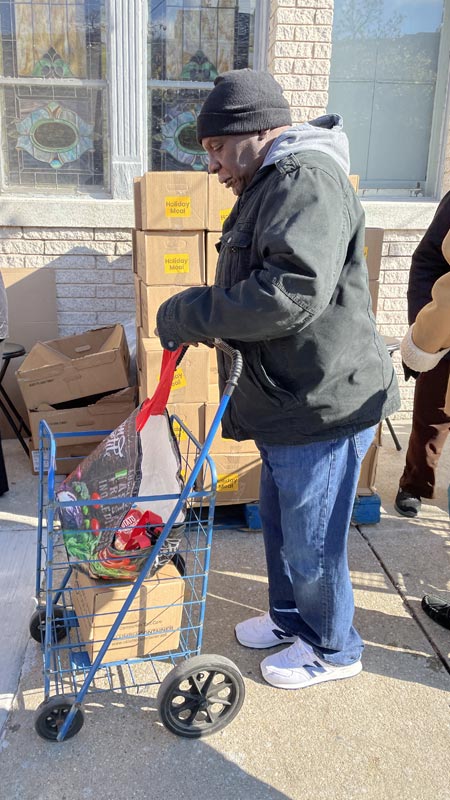 man stands on sidewalk with his cart to pickup holiday food