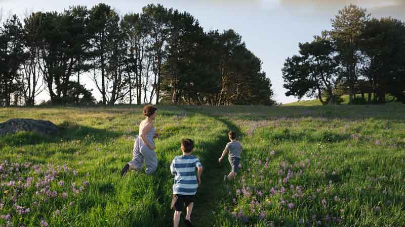 mother running in green field with two boys