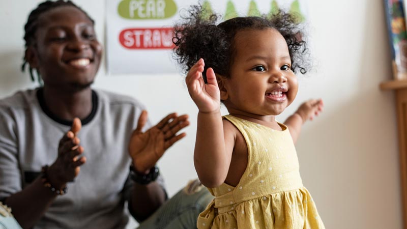 black parent claps while their toddler walks