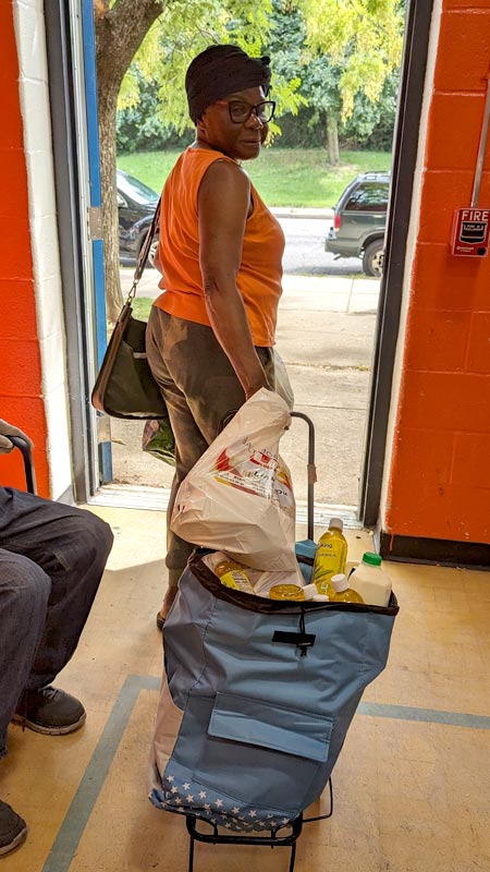 woman walking out door pulling cart of food behind