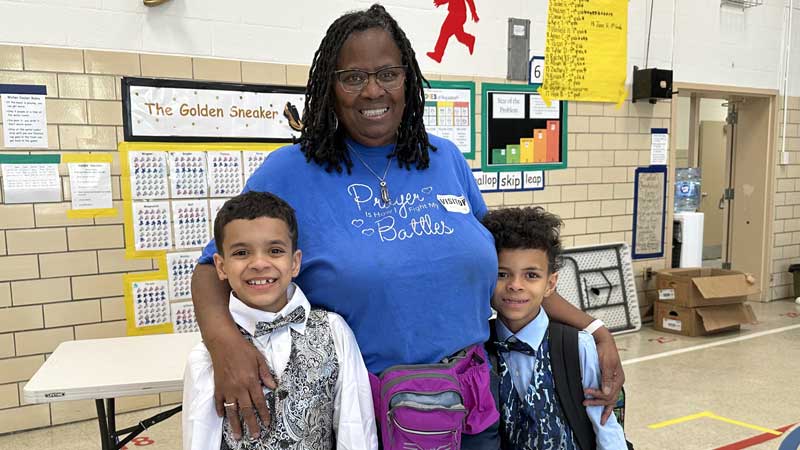 smiling black woman standing in school with two happy elementary school boys