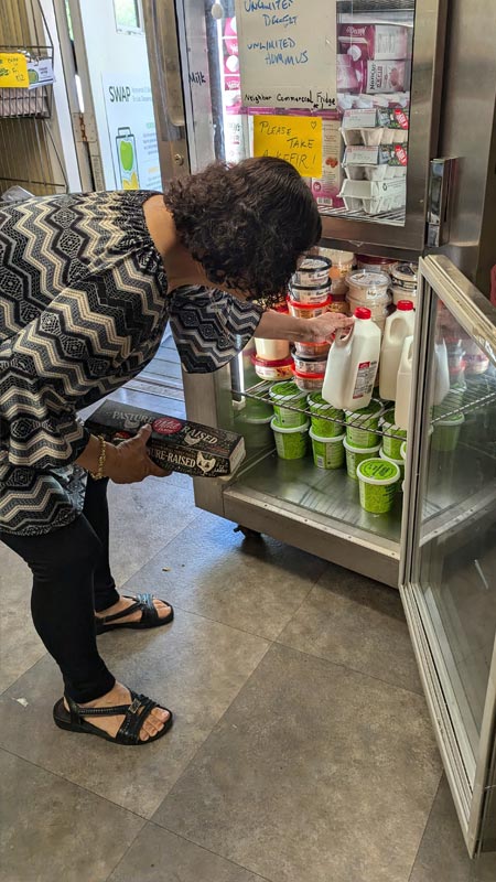 lady grabs cold food items from a short refrigerator