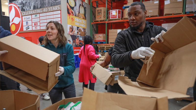 caucasian woman and black man volunteer by breaking down boxes together in the Maryland Food Bank warehouse