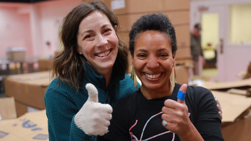 two women volunteers give a thumbs up with big smiles
