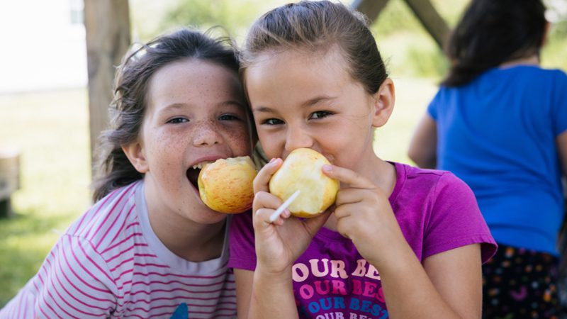two elementary schoolgirls laughing while eating apples