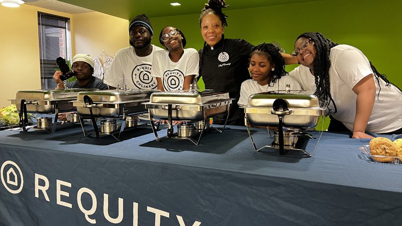 Bria Evans standing at a Requity Foundation prepared hot food table with her crew
