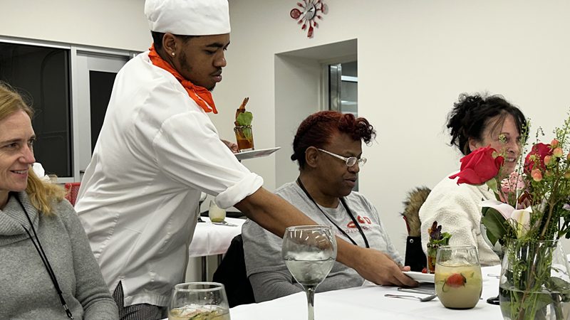 one FoodWorks student serving food to a table of three happy and hungry women