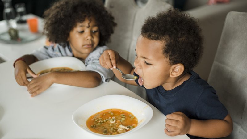 little girl and boy sitting at table eating soup