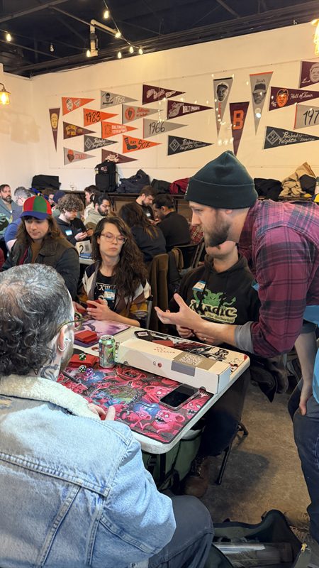 Adam Melfa talks to a table of people at the Peabody Heights Brewery Magic the Gathering event